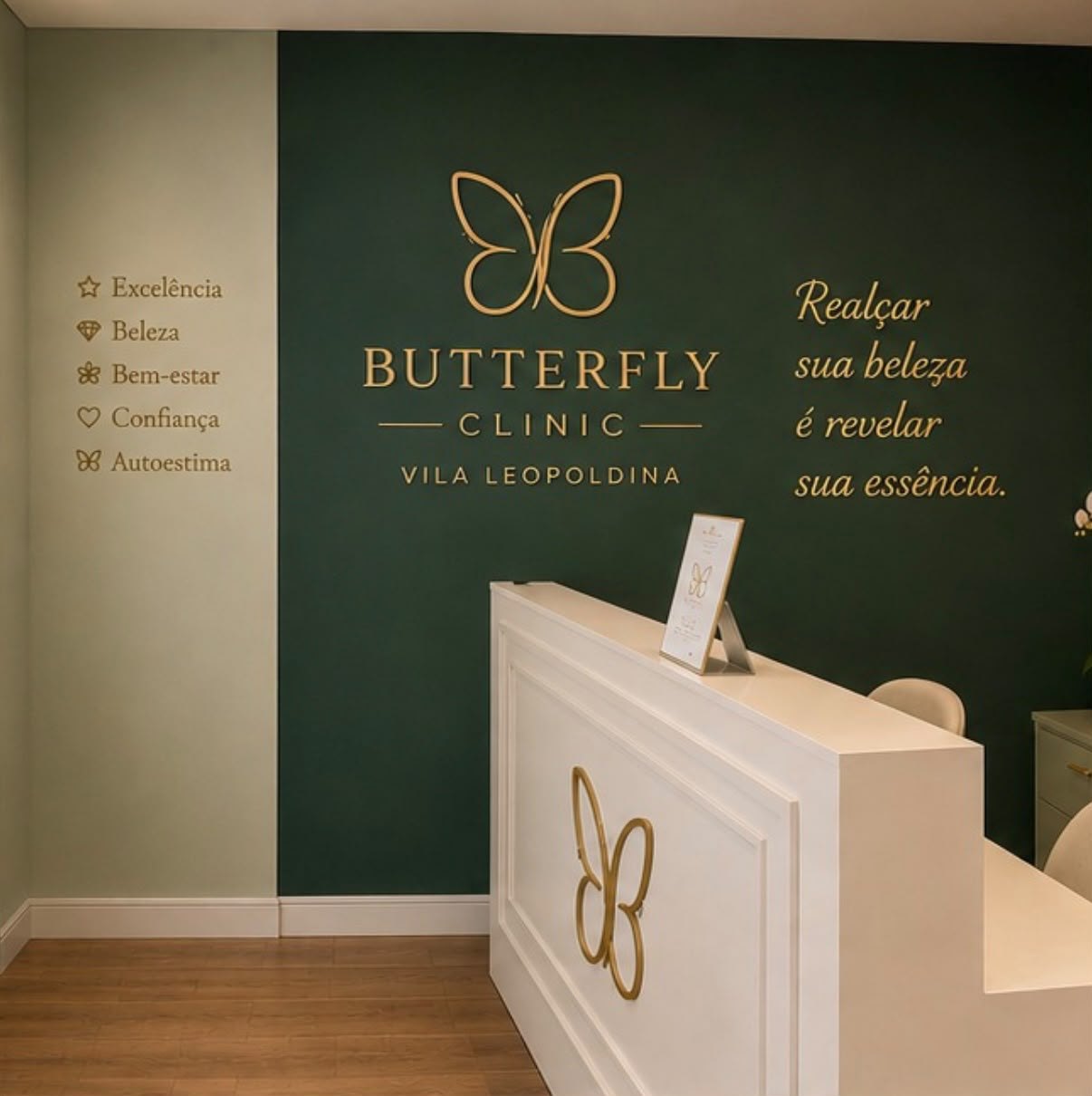 Recepção da Butterfly Clinic com parede verde, logo dourado e a frase Realçar sua beleza é revelar sua essência